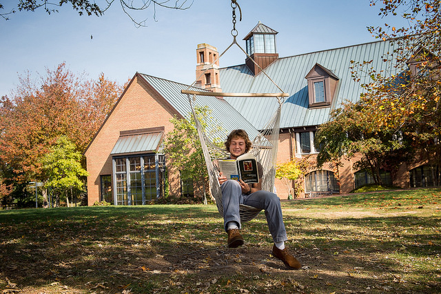 a SMCM student sitting on a hammock reading a book outside one of the college buildings