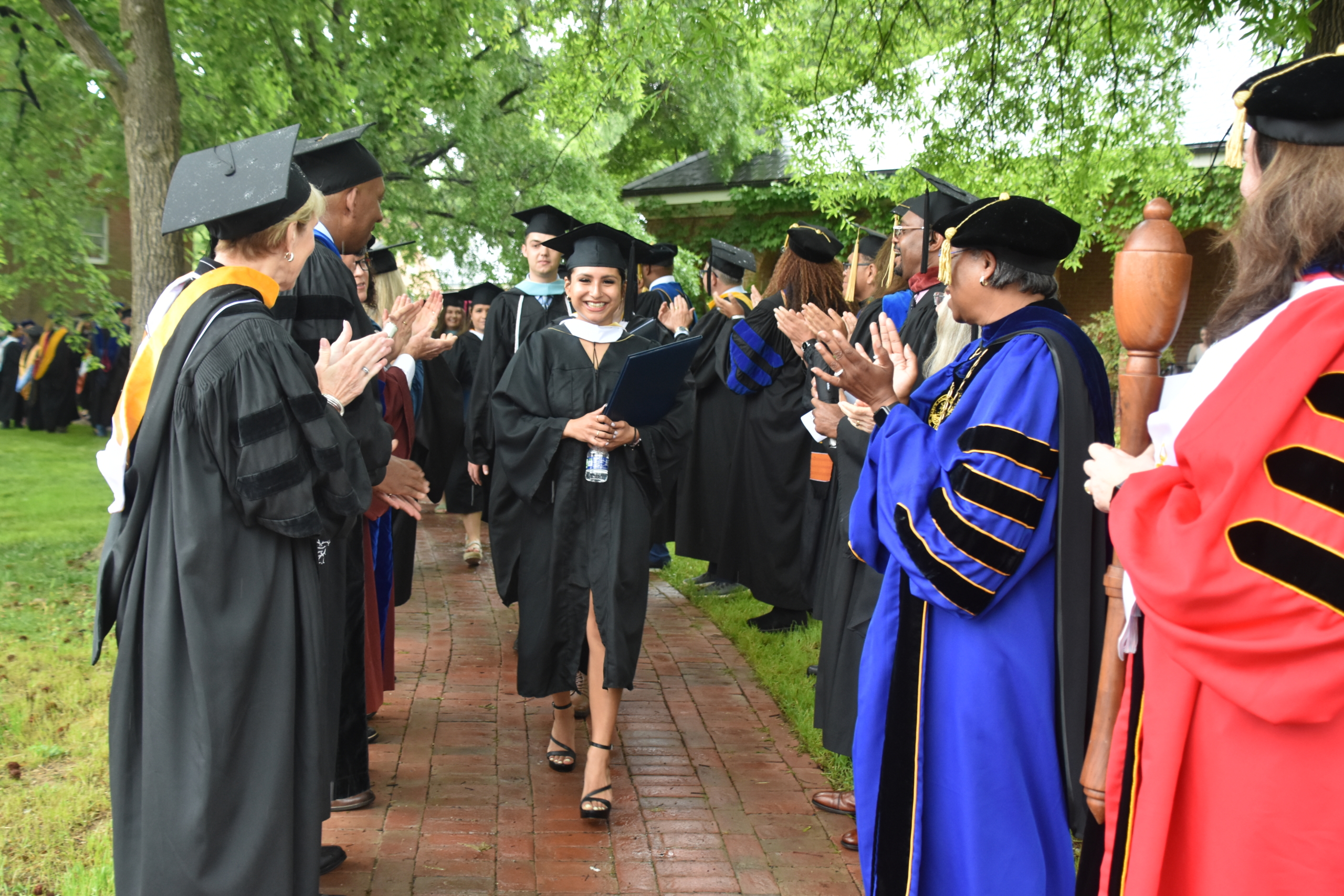 An image of administrators and faculty in two lines, outdoors on the campus of St. Mary's College of Maryland applauding students walking past wearing their cap and gown.