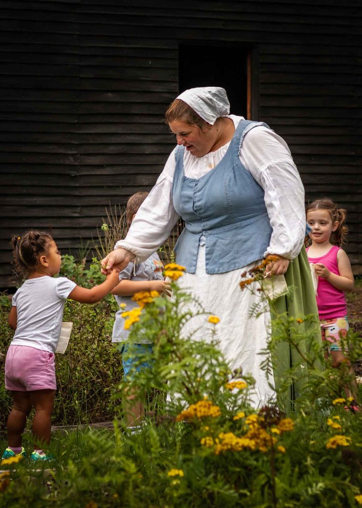 A woman dressed in historical costume hands a flower to a young girl