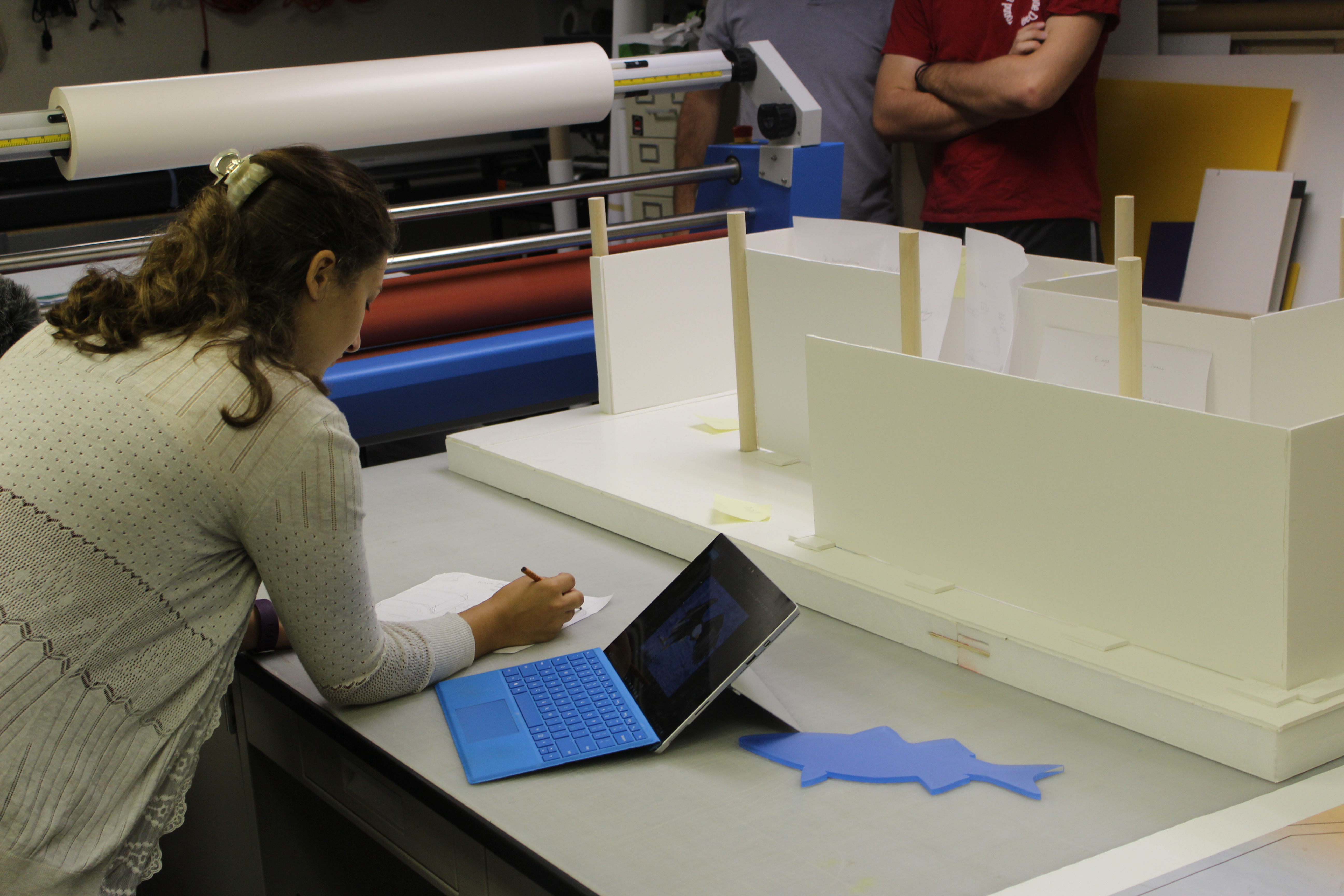 A student designing a building with paper and pencil with the building model in front of her